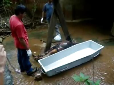Gagging Man in Blue Shirt moves a Bloated Corpse into a Coffin